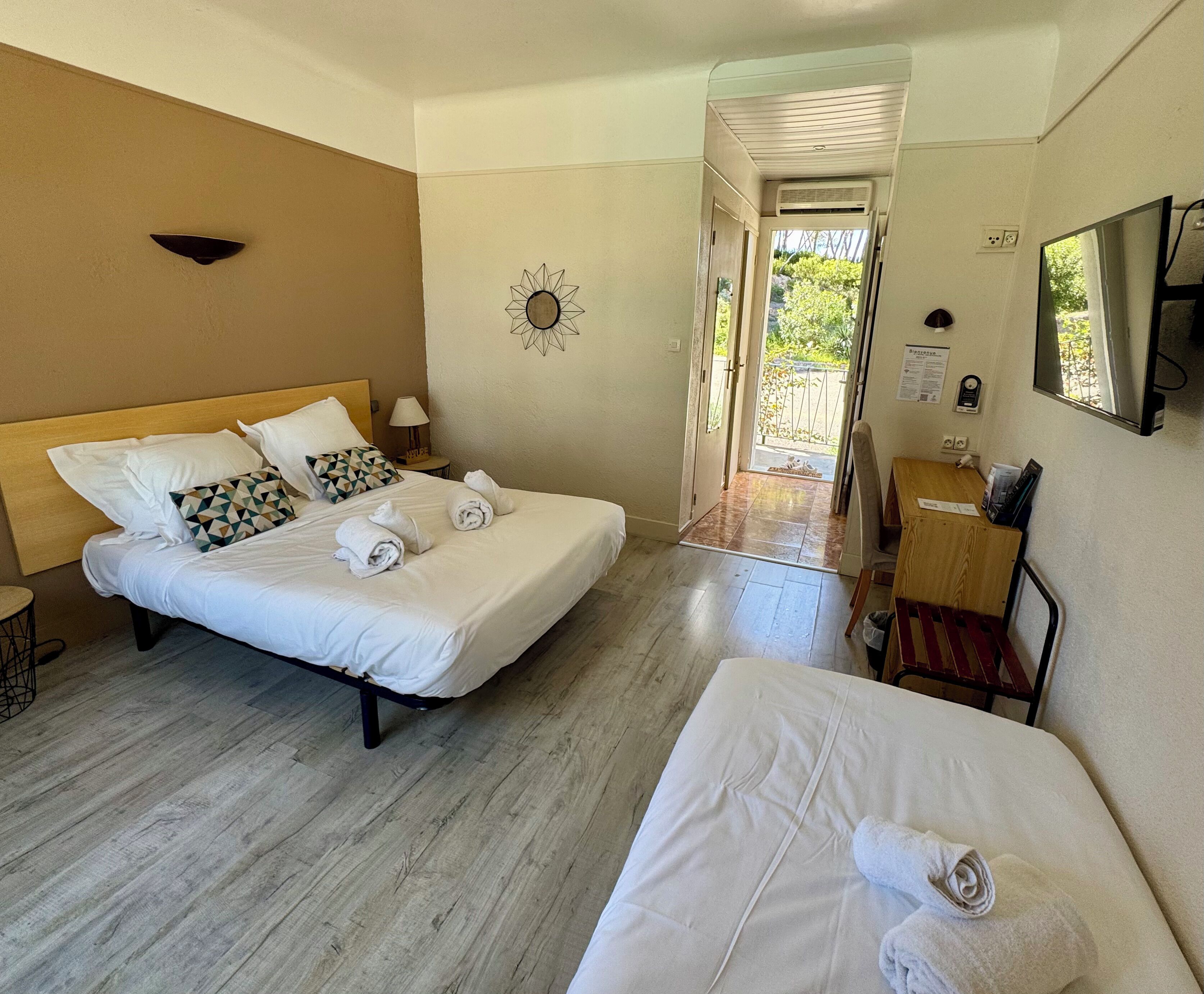 A hotel room with two beds, a desk, a chair, a lamp, and a door leading outside.