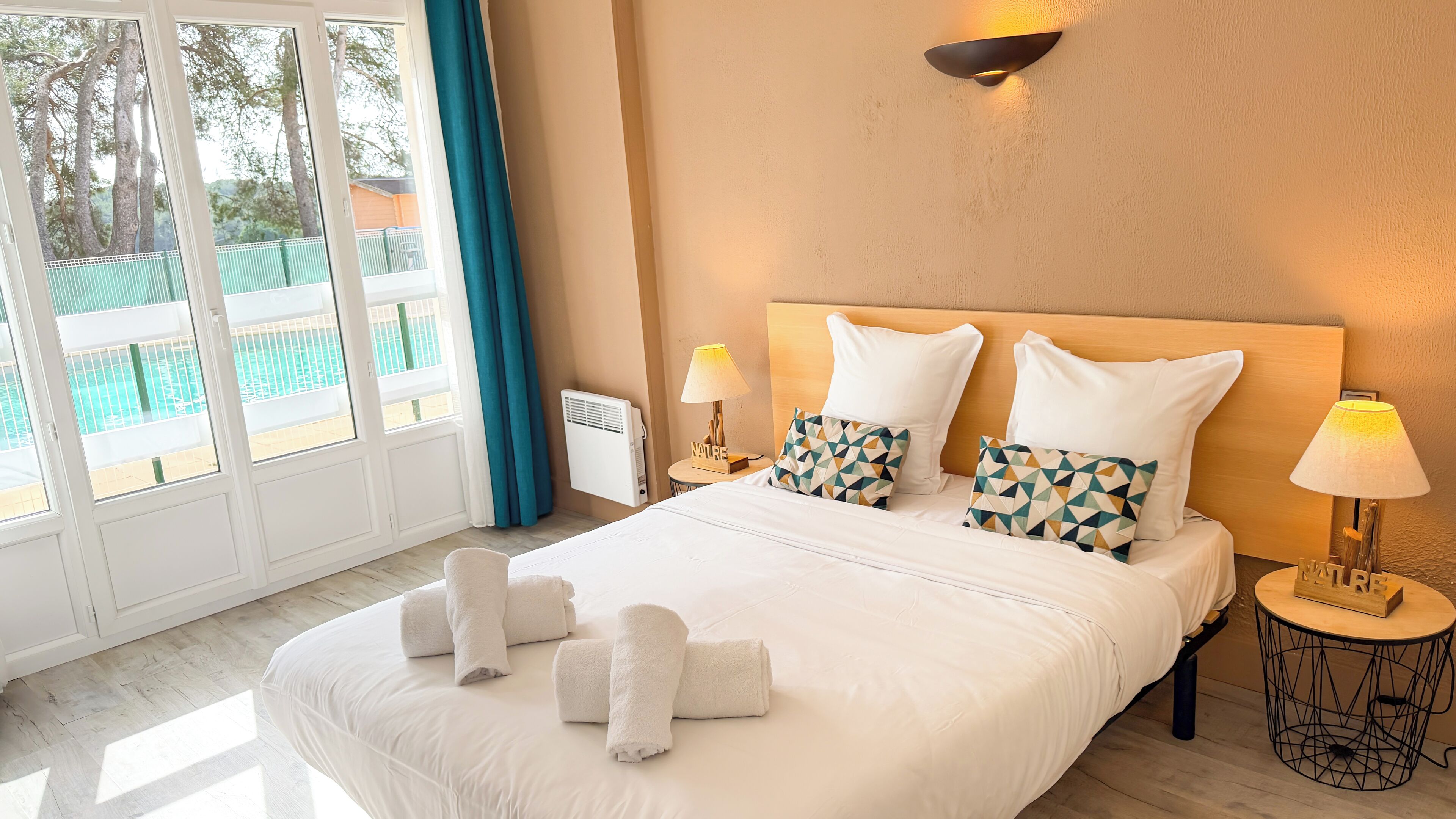 A hotel room with a large bed, two bedside lamps, a view of a pool, and a window with curtains.