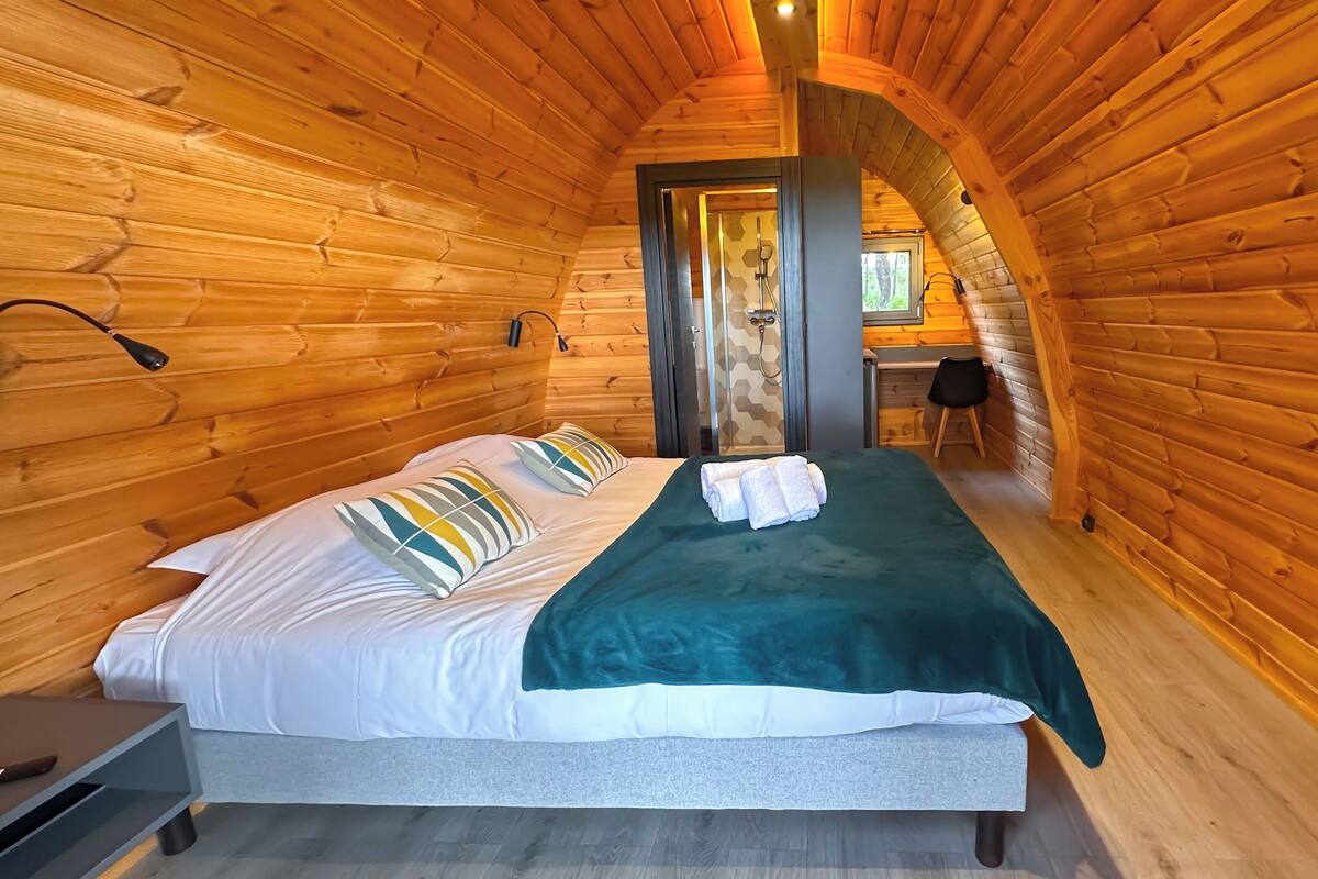 A cozy log cabin bedroom with a bed, pillows, a green blanket, and a shower area.