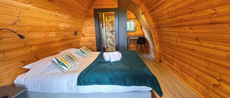 A cozy log cabin bedroom with a bed, pillows, a green blanket, and a shower area.