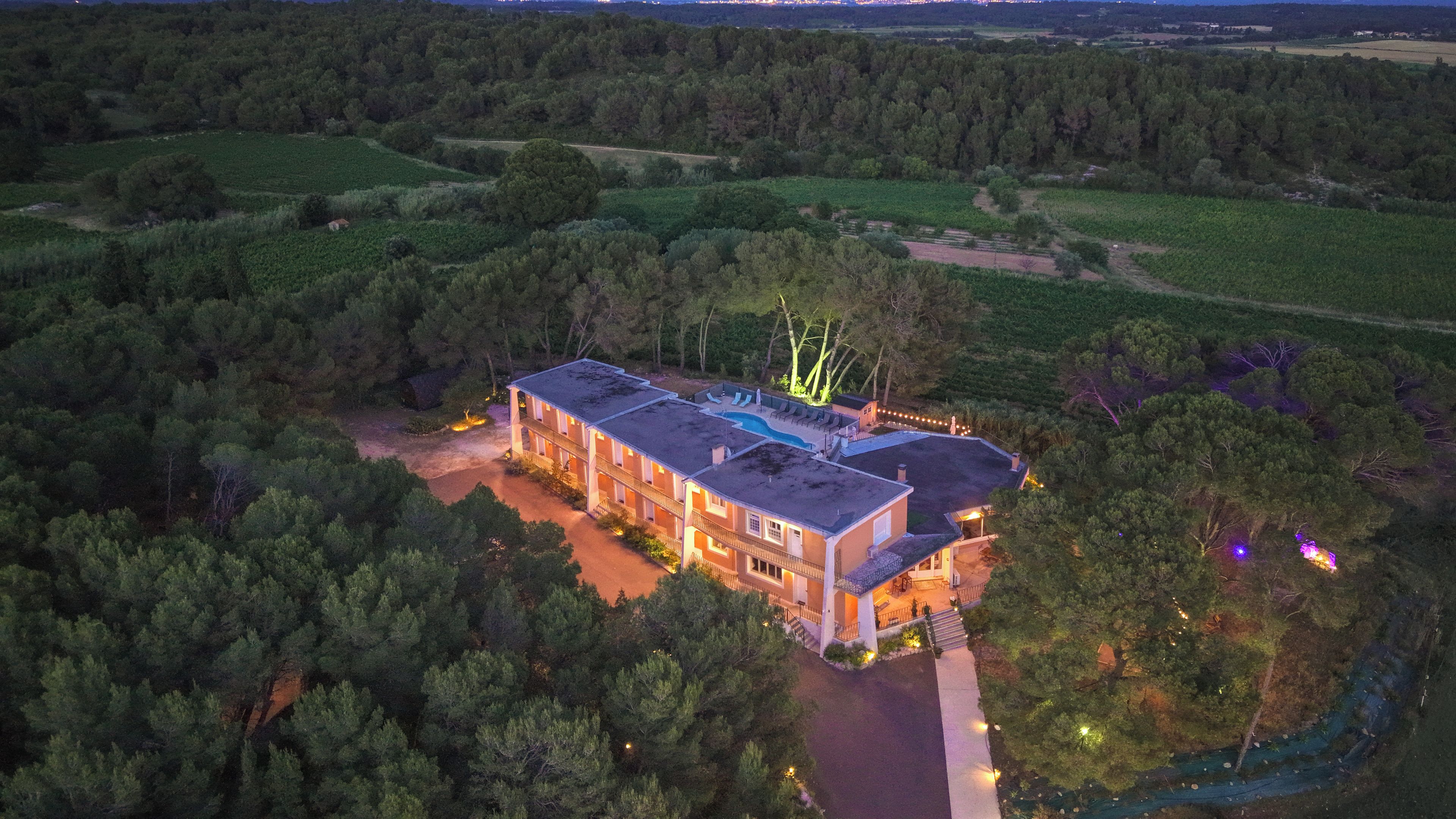 Un edificio grande de varios pisos con piscina y zona de estar al aire libre, rodeado de un bosque denso.