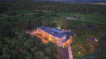 Un edificio grande de varios pisos con piscina y zona de estar al aire libre, rodeado de un bosque denso.