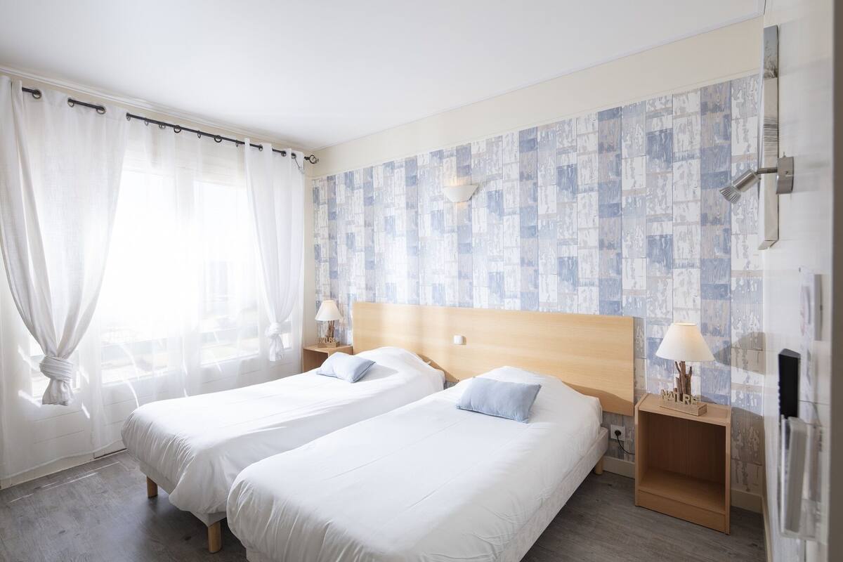 A hotel room with two beds, a wooden headboard, a nightstand with a lamp, and a patterned wall.