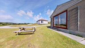 Ein Gebäude mit einem großen Fenster, einem Picknicktisch und einem kleinen Haus im Hintergrund.