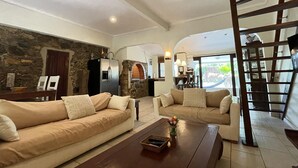 A spacious living area with a stone wall, a kitchen with an archway, and a balcony with a view. - Charming Aruban house (Noord)