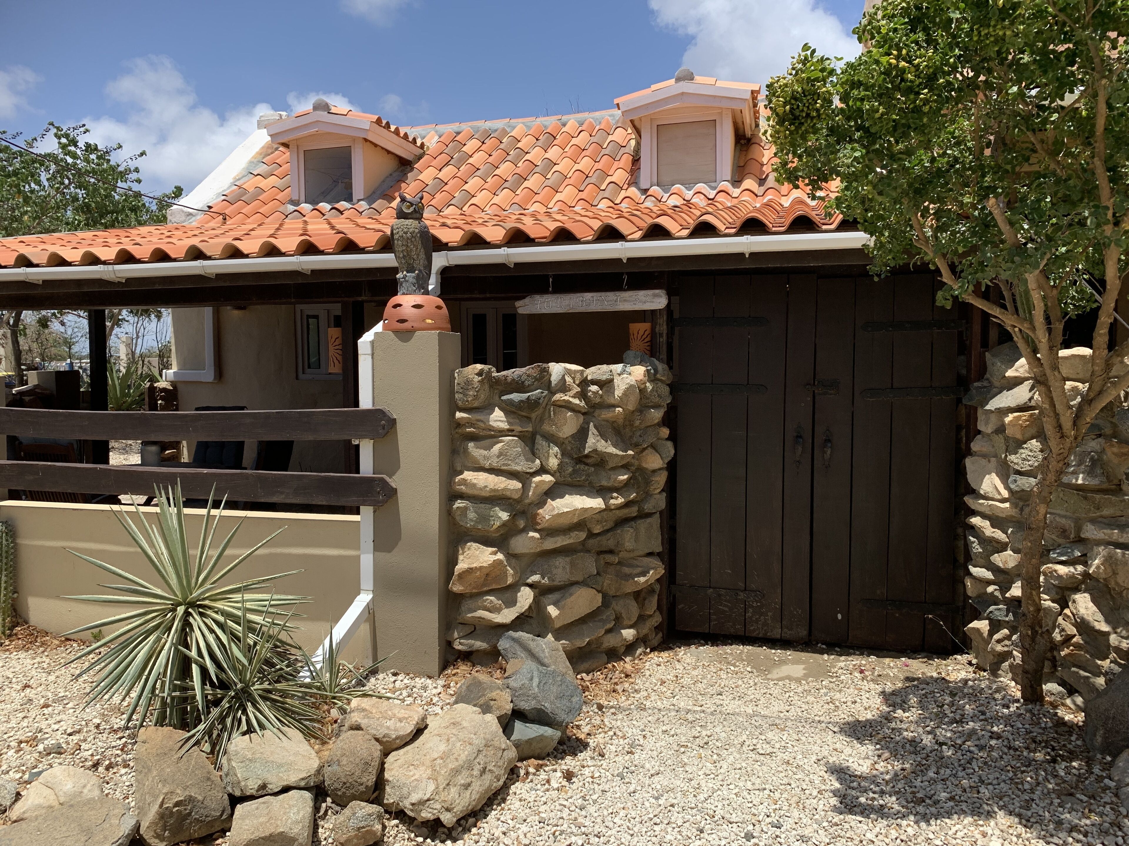 Una casa con un muro de piedra, un portón de madera y una planta de cactus en el jardín.