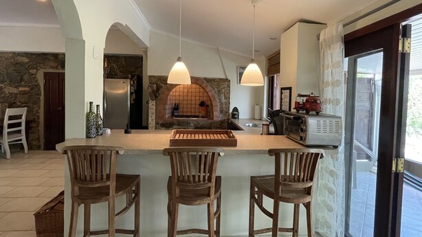 A spacious kitchen with a large island, wooden chairs, pendant lights, and a stone wall backsplash. - Charming Aruban house (Noord)