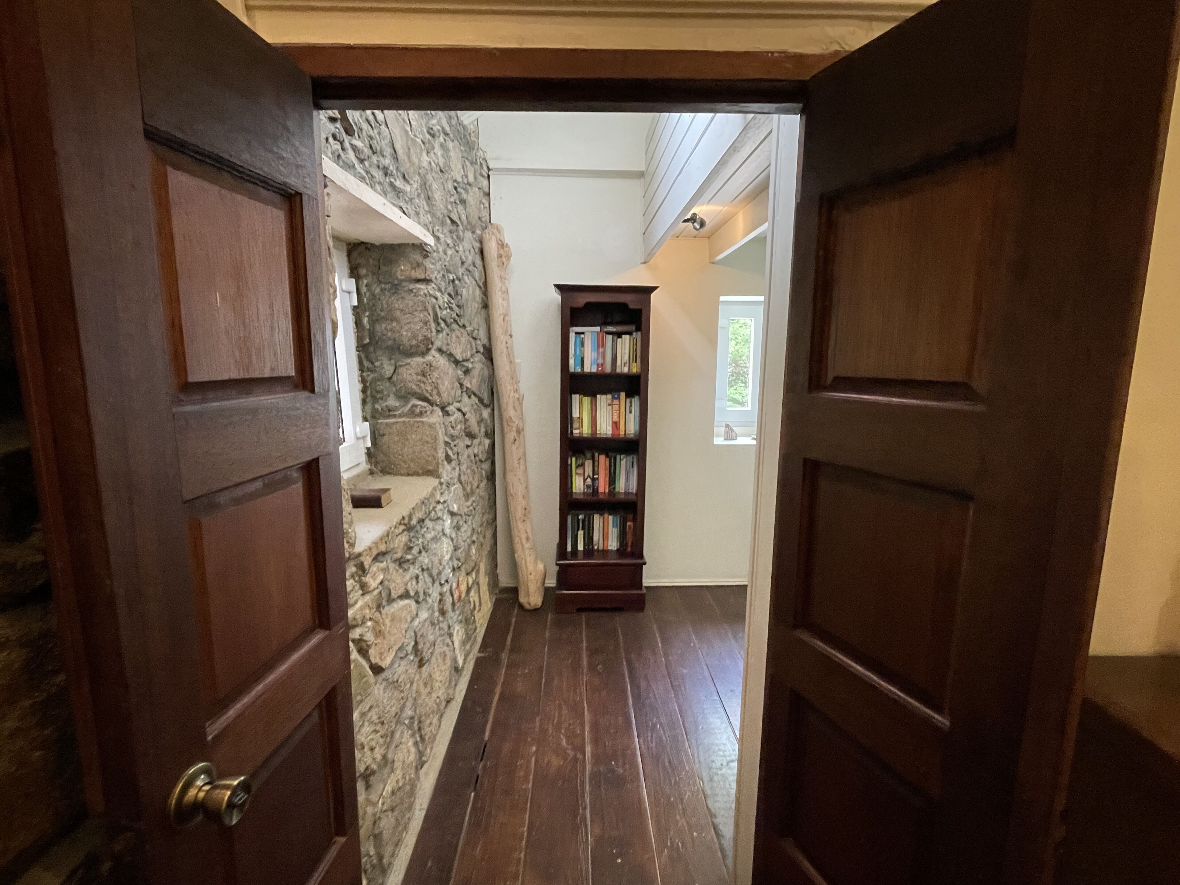 A hallway with a stone wall, wooden floor, and a bookshelf.