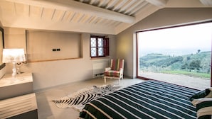 Un dormitorio con una cama grande, un alfombra de cebra, una silla, una ventana y vistas al campo.