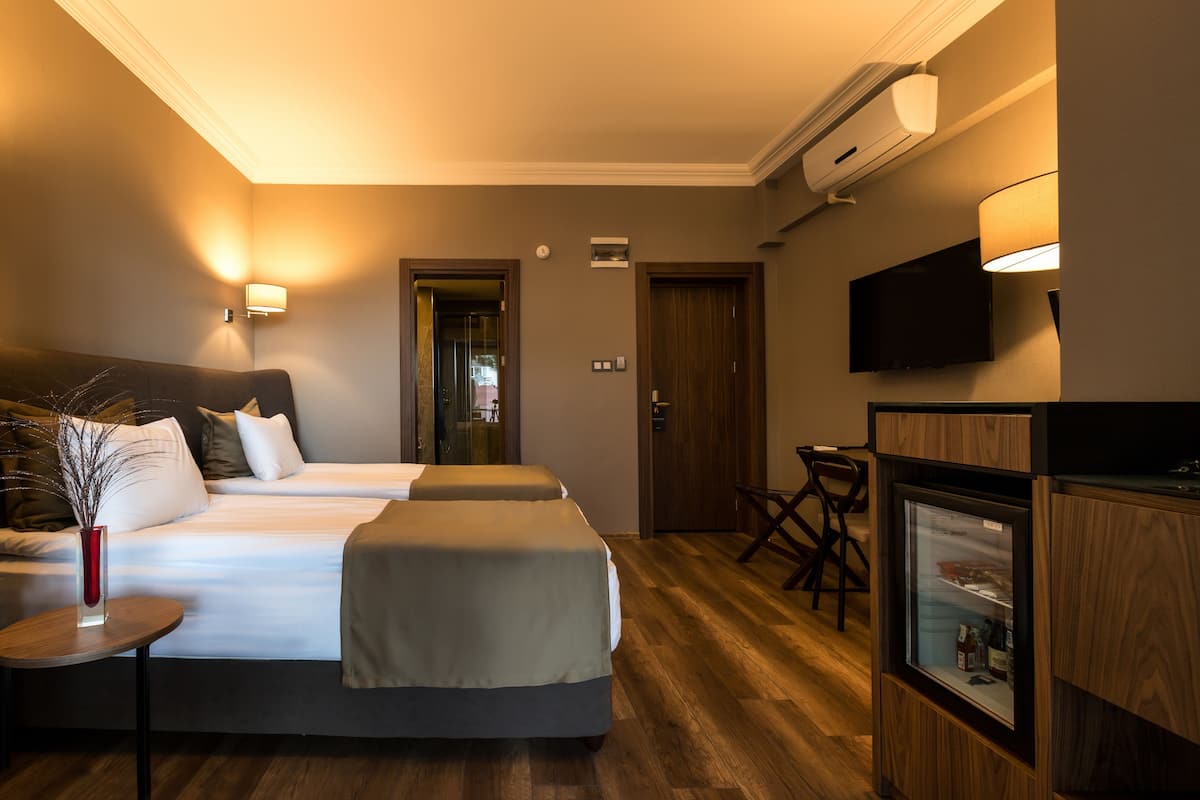 Una camera d'albergo con due letti, un tavolino, una sedia, una TV e un minibar.