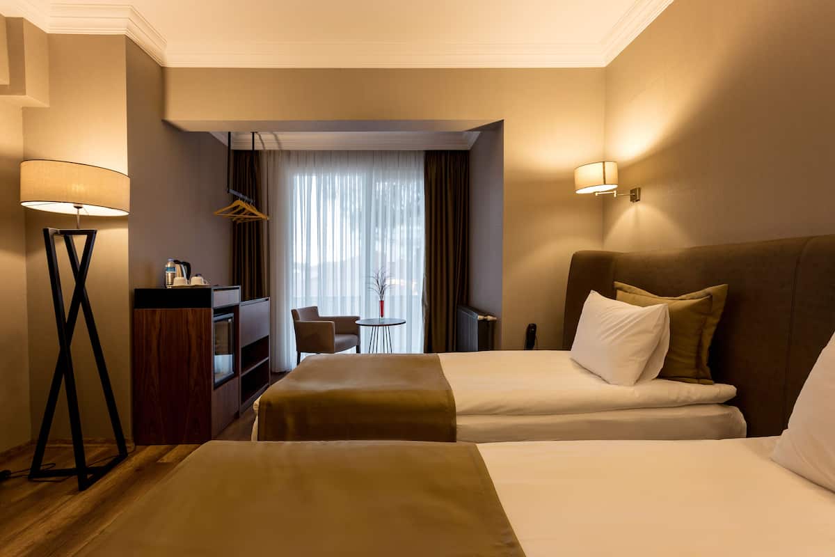 Camera d'albergo con due letti, una scrivania, una sedia e una lampada.