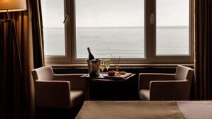 Quarto de hotel com vista para o mar, uma mesa com champanhe, copos e petiscos.