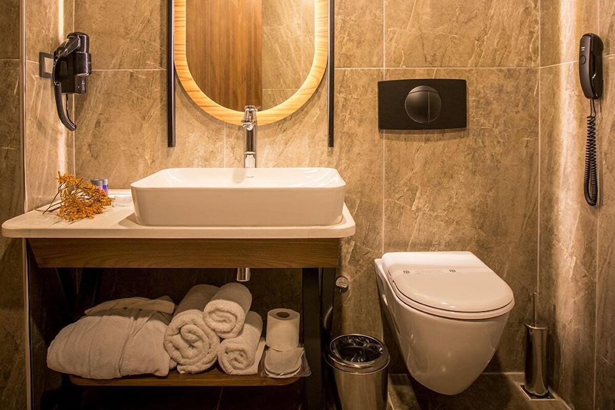 Un bagno moderno con lavabo in marmo, uno specchio grande, un water e un cestino.
