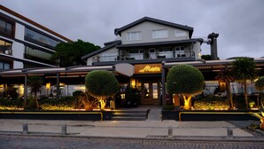 Um hotel com design moderno, destacando uma entrada imponente com letreiro neon, área externa coberta e paisagismo bem cuidado.