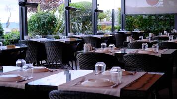 Un restaurante con mesas dispuestas para comer, que cuenta con sillas de mimbre y vistas al exterior con vegetación.