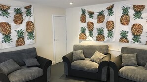 A room with two sofas and a chair, a white door, and walls decorated with pineapple patterns. - Geise Farm Services (Thurso)