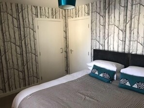 A bedroom with a bed, two doors, and a wall with a tree pattern.