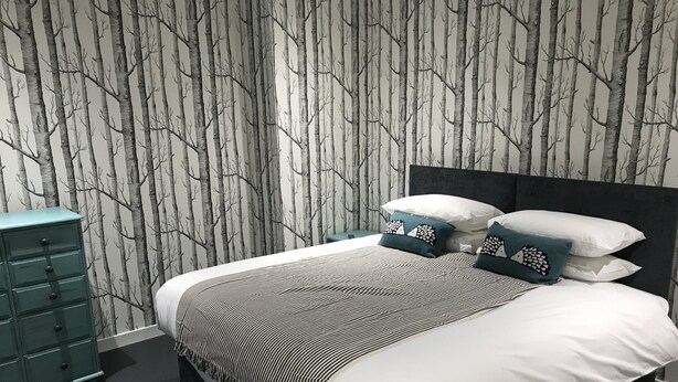 A bedroom with a bed, a dresser, and a wall with a tree pattern. - Geise Farm Services (Thurso)