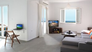 A modern living room with a grey sofa, a wooden chair, a TV, and a laptop on a shelf. - Evriali Luxury on the beach (Plaka Naxos)