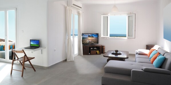 A modern living room with a grey sofa, a wooden chair, a TV, and a laptop on a shelf.
