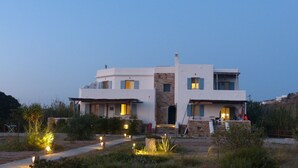 A modern two-story house with a stone facade, multiple windows with shutters, and a well-lit entrance. - Evriali Luxury on the beach (Plaka Naxos)