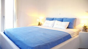 A neatly made bed with a blue bedspread and white pillows, flanked by two bedside tables with lamps. - Evriali Luxury on the beach (Plaka Naxos)