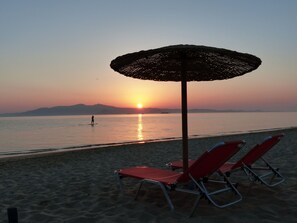 A beach scene with a sunset, a beach umbrella, and two red lounge chairs.