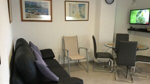 A living room with a black sofa, two chairs, a small table, and a TV on a stand.