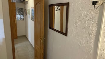 Un pasillo con una puerta de madera, un espejo enmarcado y un enchufe en la pared.