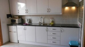 A compact kitchen with white cabinets, a microwave, a kettle, and a sink.