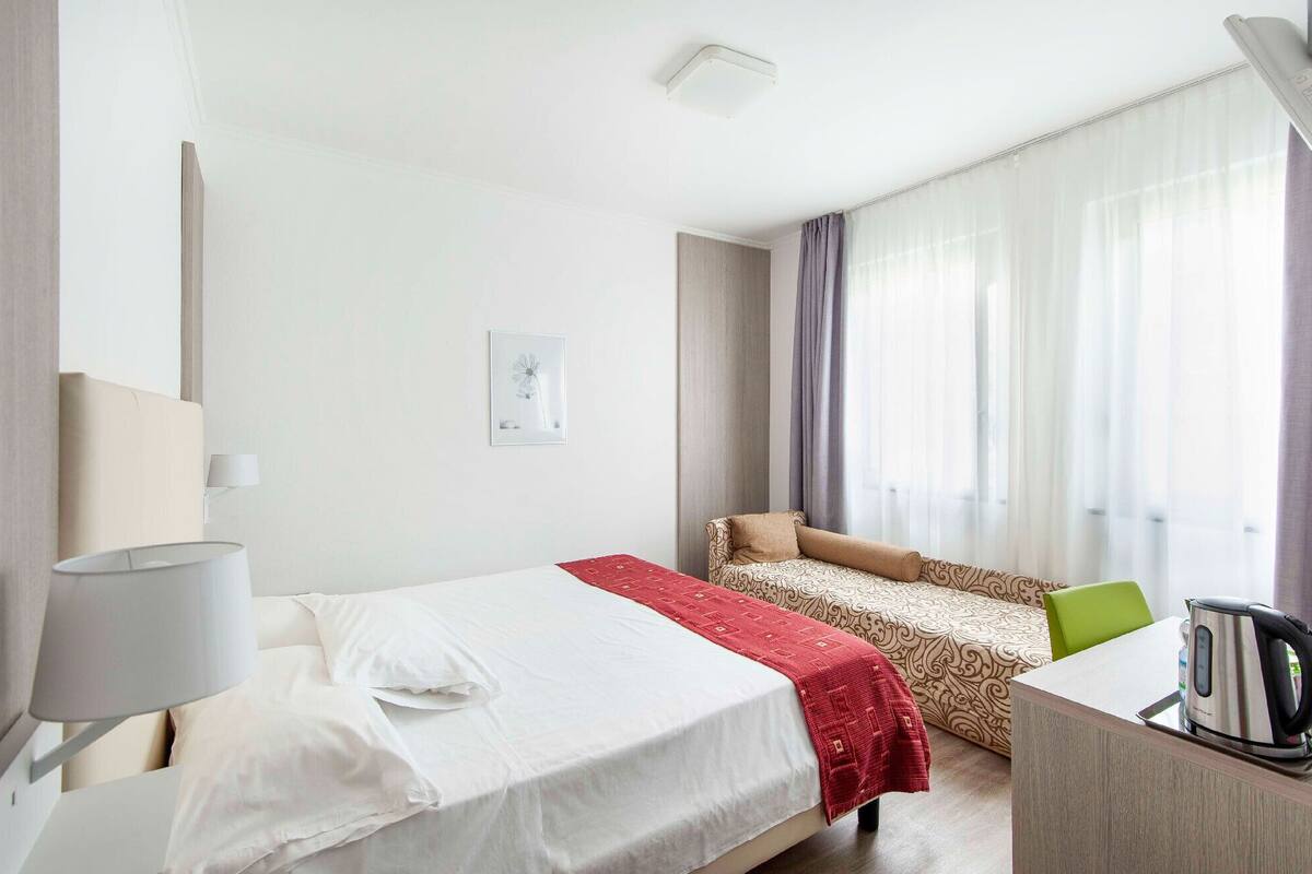 Una camera d'albergo con un letto, una scrivania, una sedia, una lampada e una finestra con tende.