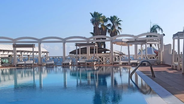 A pool with lounge chairs and umbrellas, surrounded by white structures and palm trees. - La Corvetta (Monopoli)