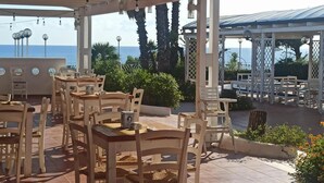An outdoor patio with wooden tables and chairs, a pergola, and a view of the sea. - La Corvetta (Monopoli)