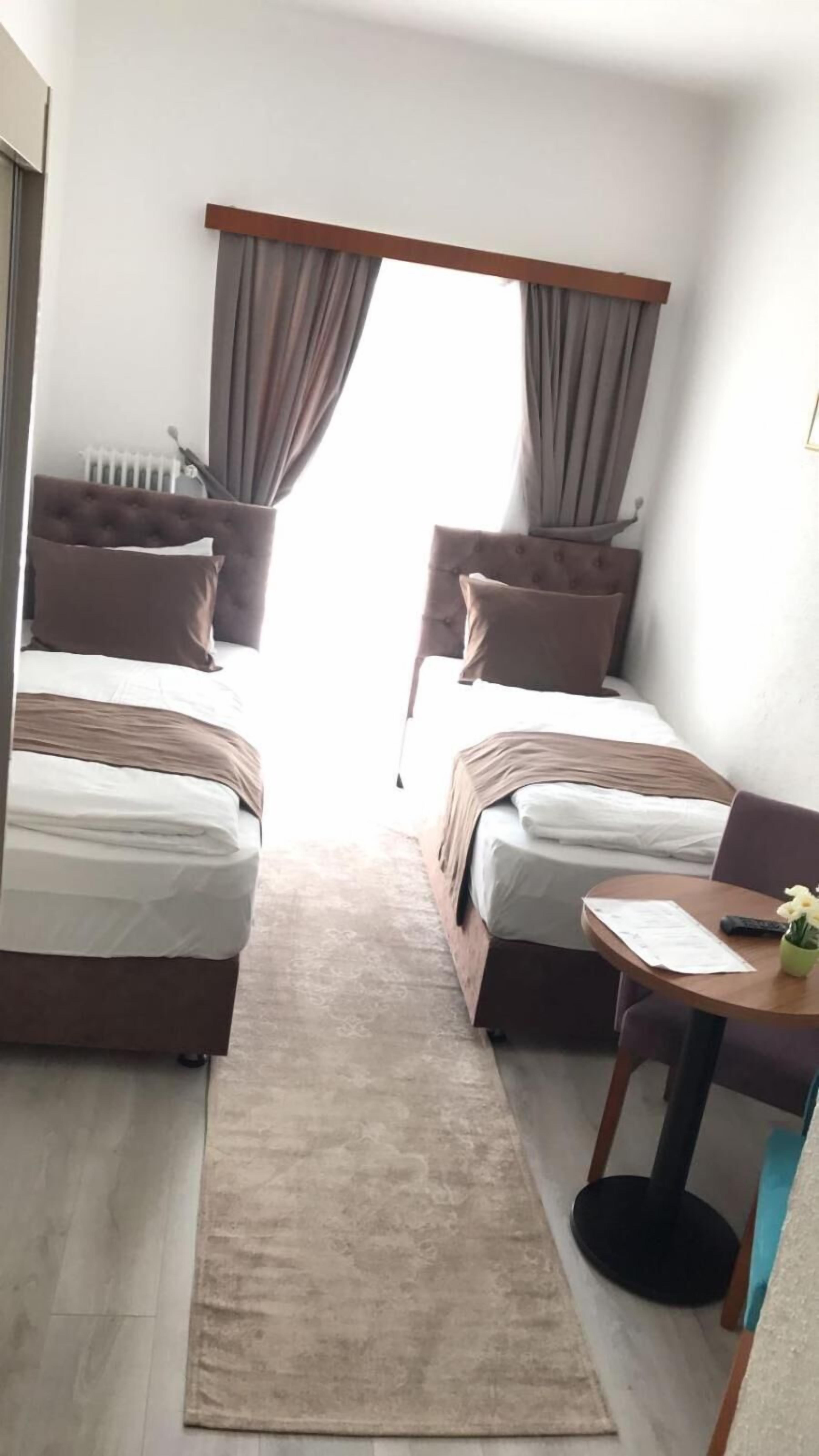 A small, modern hotel room with two beds, a small table, and a chair.
