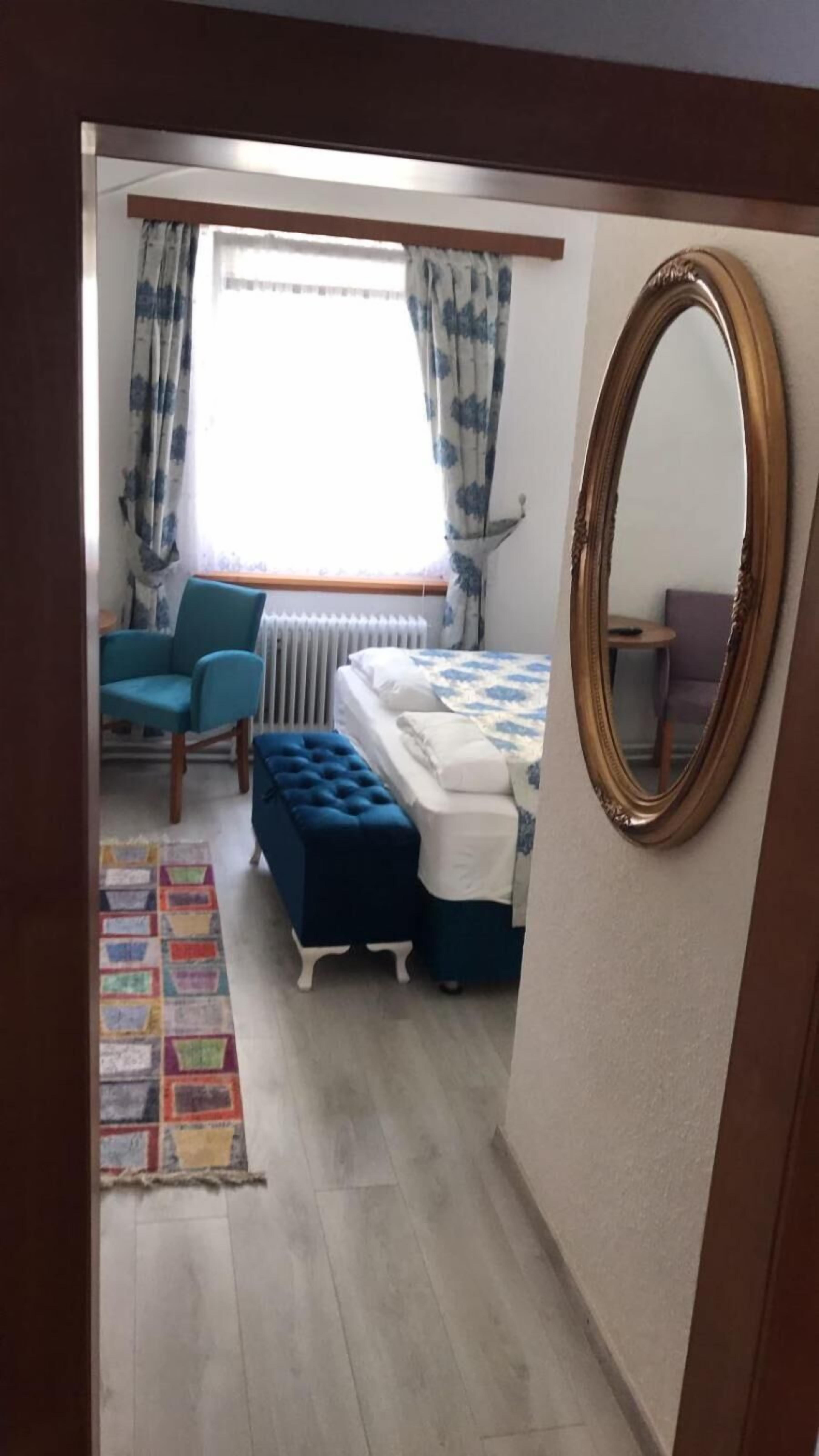Una camera da letto con un letto, una sedia, un tavolino, uno specchio e una finestra con tende.