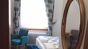 Una camera da letto con un letto, una sedia, un tavolino, uno specchio e una finestra con tende.