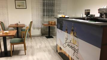 A hotel reception area with a wooden reception desk, a coffee machine, and a dining area with a table and chairs.