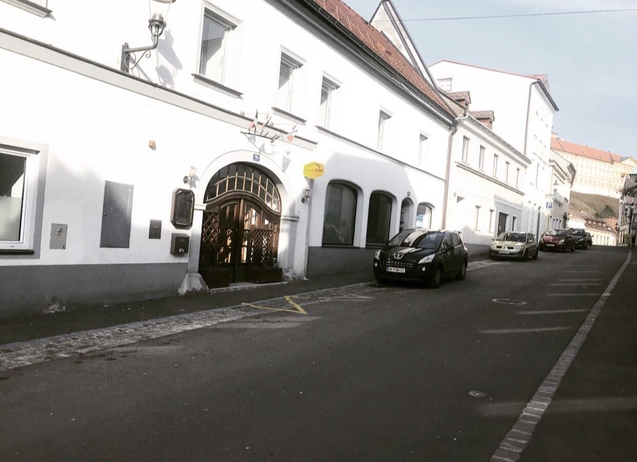 A street with a white building featuring a large arched entrance and several parked cars.