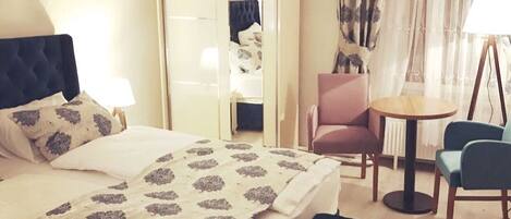 A hotel room with a bed, a chair, a small table, and a mirror.
