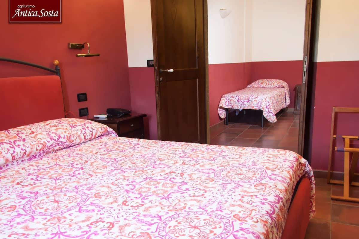 A hotel room with a large bed, a bedside table, a chair, and a door leading to another room.