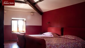 Un dormitorio con dos camas, una pared roja y un ventanal con luz natural.