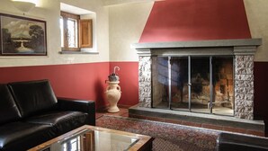 Una sala de estar con chimenea, un sofá de cuero negro, una mesa de centro de vidrio y una decoración en colores rojo y blanco.