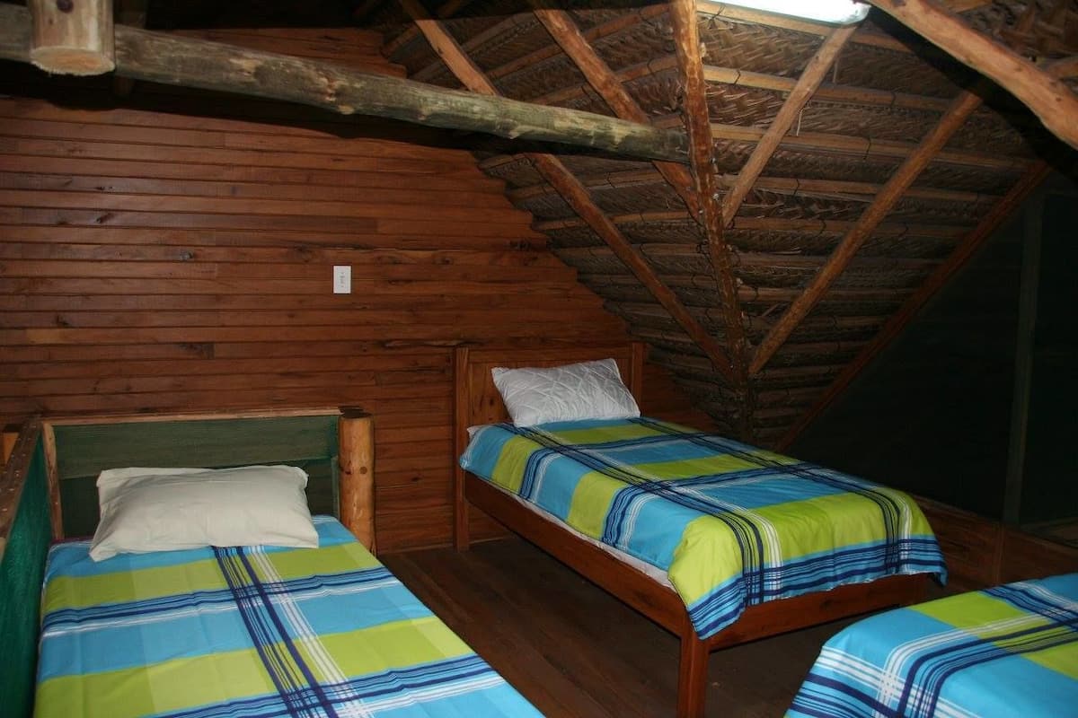Una habitación pequeña y rústica con paredes de madera y techo inclinado. Hay dos camas individuales con ropa de cama a rayas.