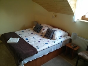 A bedroom with a bed, pillows, a blanket, a bedside table with a lamp, and a chair.