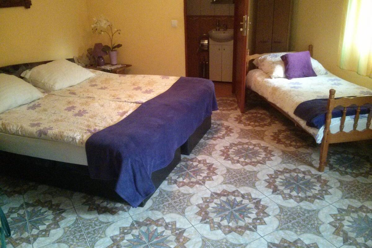 A room with two beds, a bathroom, and a tiled floor.