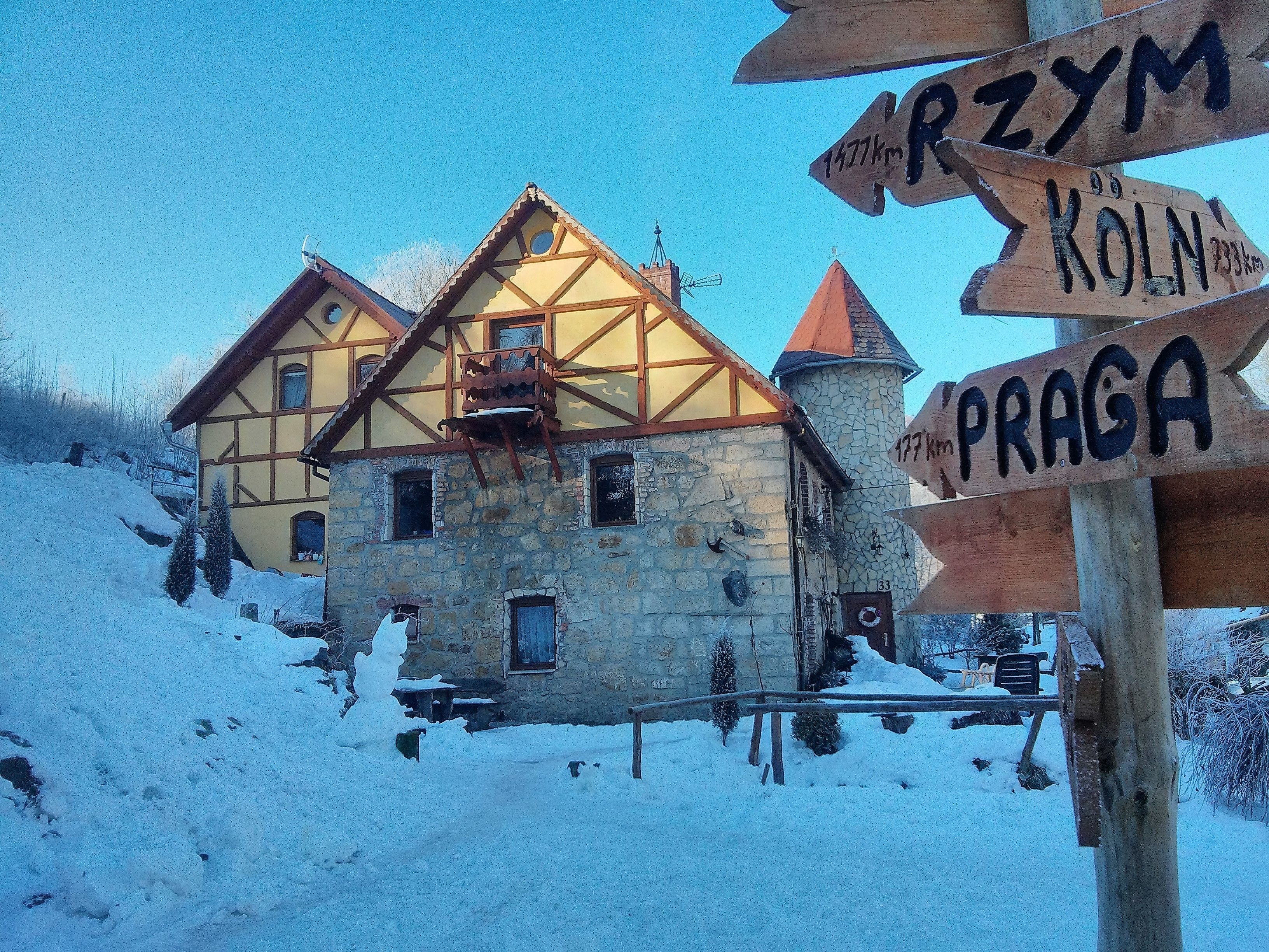 A traditional half-timbered house with a stone base and a wooden upper structure, surrounded by snow.
