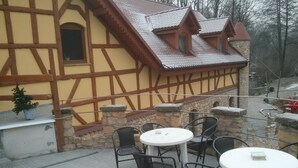 A traditional half-timbered building with stone walls and a tiled roof. There are outdoor tables and chairs arranged on a paved patio. - Zbójna Debra (Lubomierz)