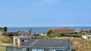 Un área residencial costera con casas, cielo despejado y el mar al fondo.