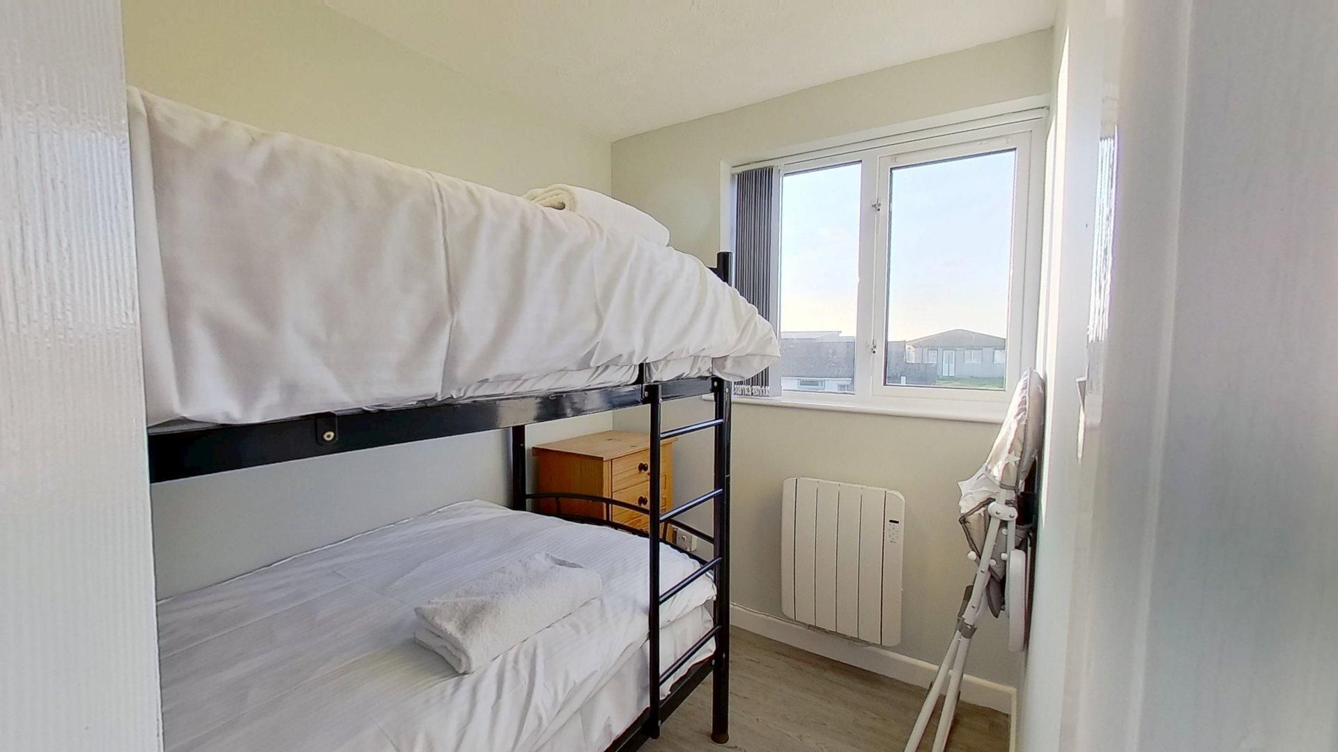 A bunk bed room with a window, radiator, and a small wooden cabinet.