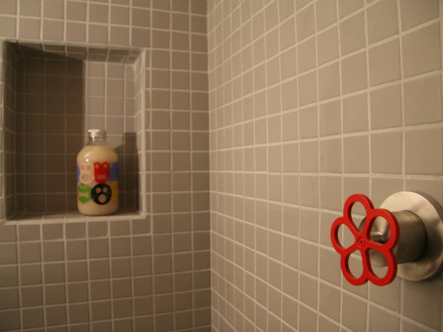 A bathroom with a tiled wall, a bottle of hand soap, and a red flower-shaped towel holder.
